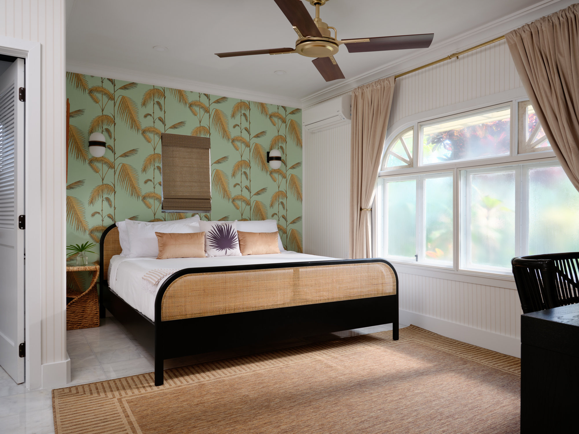 A green palm-wallpapered guest suite with a made bed and garden light